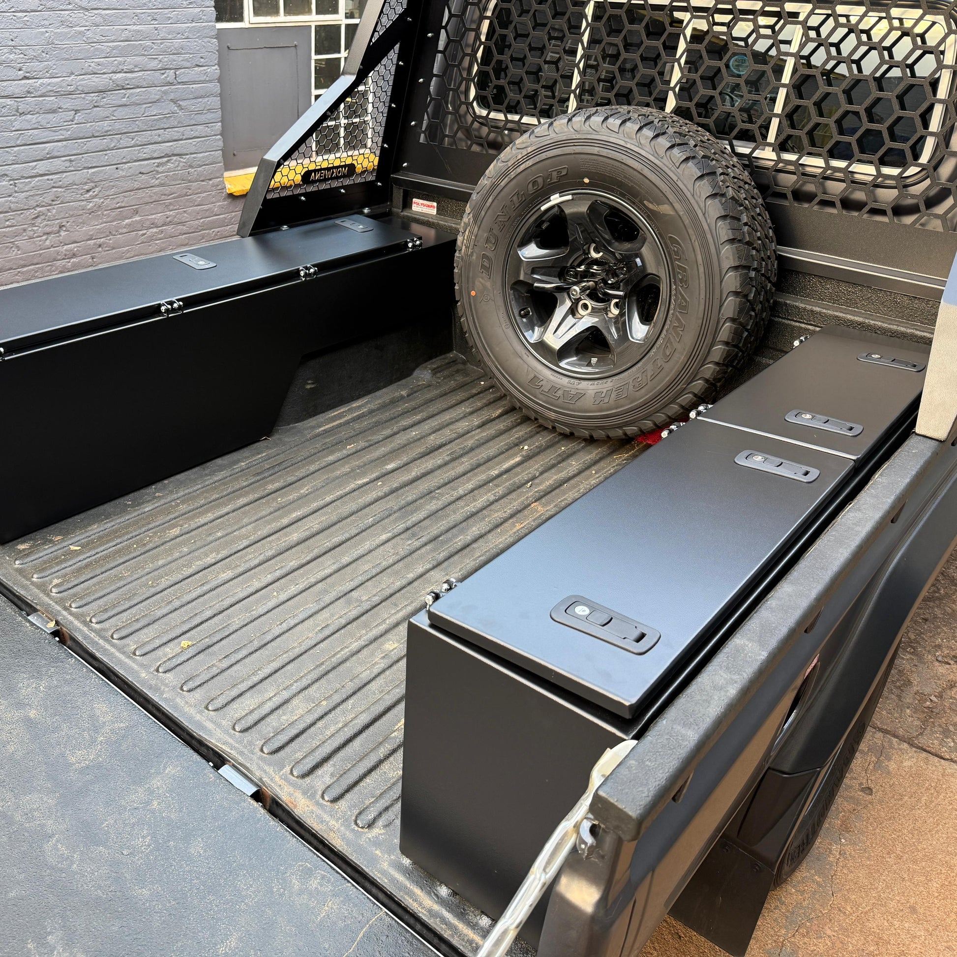 Truck bed with storage boxes and a spare tire on a concrete surface.