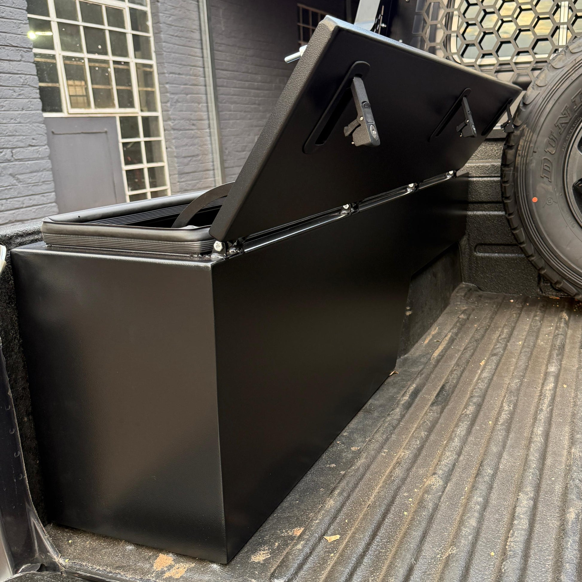 Black toolbox in the bed of a pickup truck with a building in the background