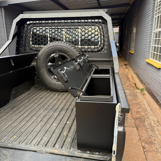 Truck bed with storage box and tire, parked next to a building.