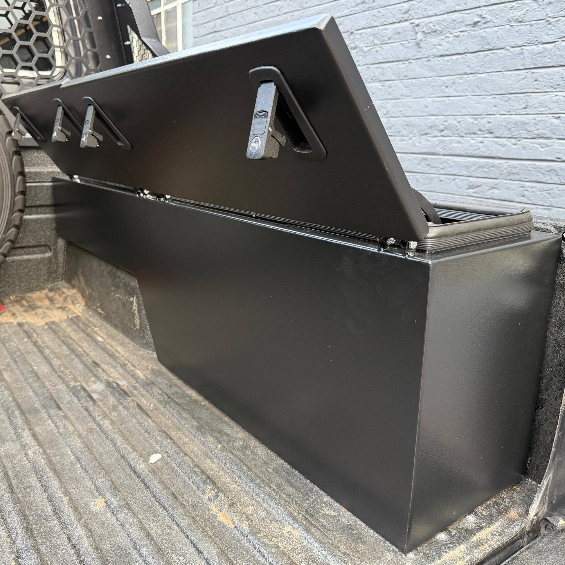 Black metal tool box on a truck bed with a brick wall background