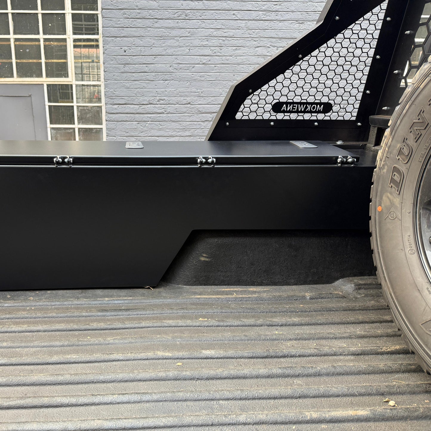 Black metal toolbox on a truck bed with a gray building in the background