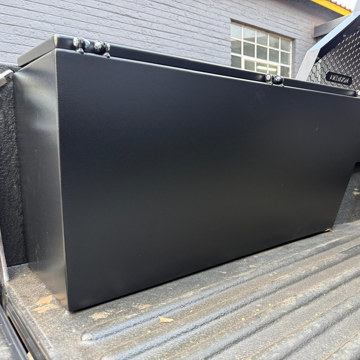 Black metal toolbox on a truck bed with a building in the background