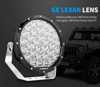 Aurora 7-inch high-lux driving lights — lens close-up with an off-road vehicle in the background